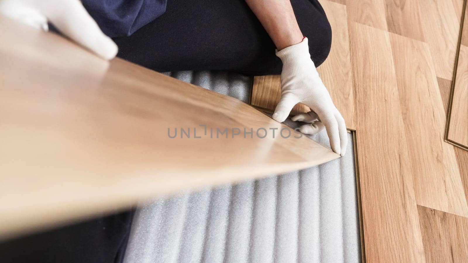 Installing laminated floor, detail on man hands holding wooden tile, over white foam base layer, blurred board tilted upward - making space for text left side