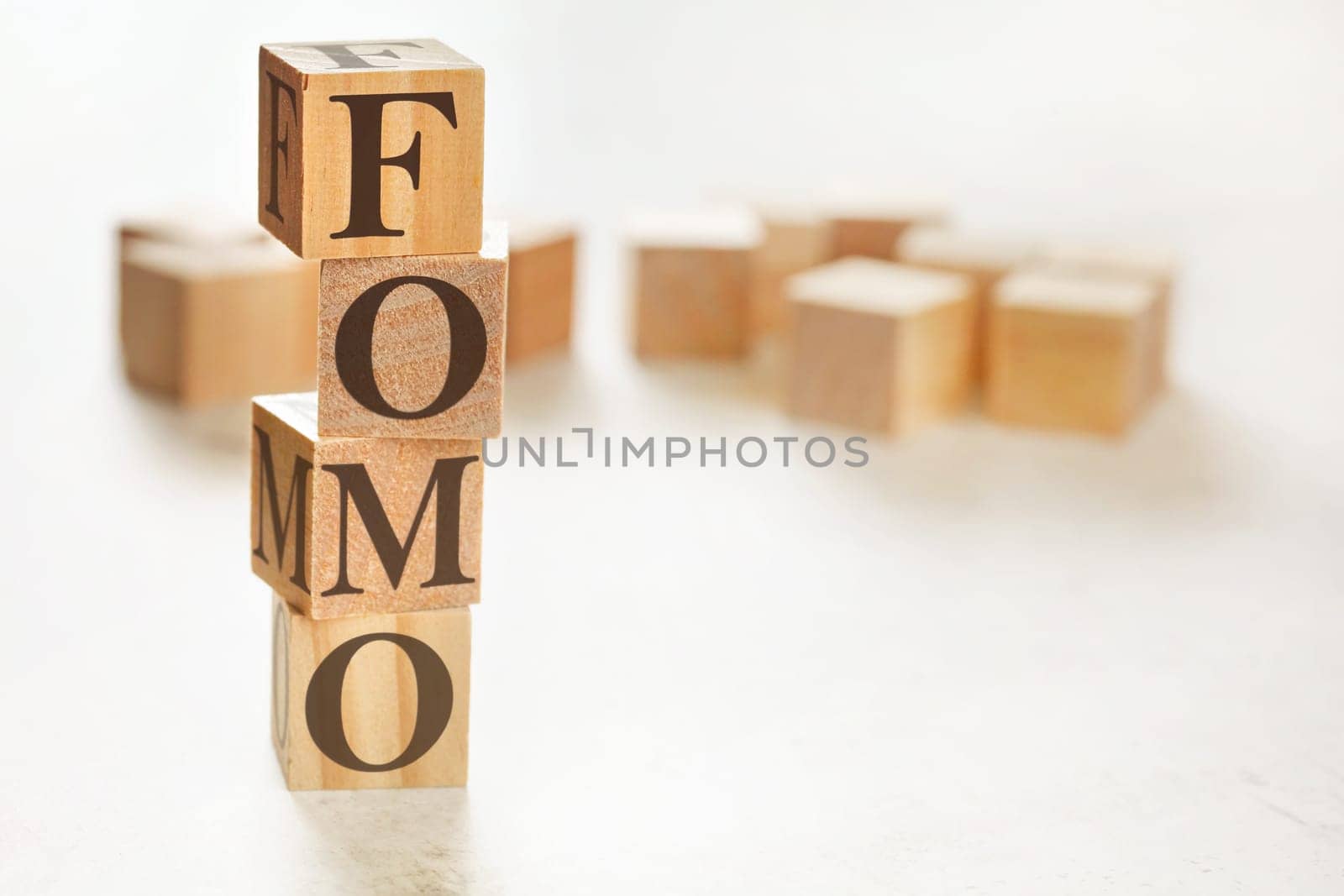 Four wooden cubes arranged in stack with letters FOMO (meaning Fear of Missing Out) on them, space for text / image at down right corner