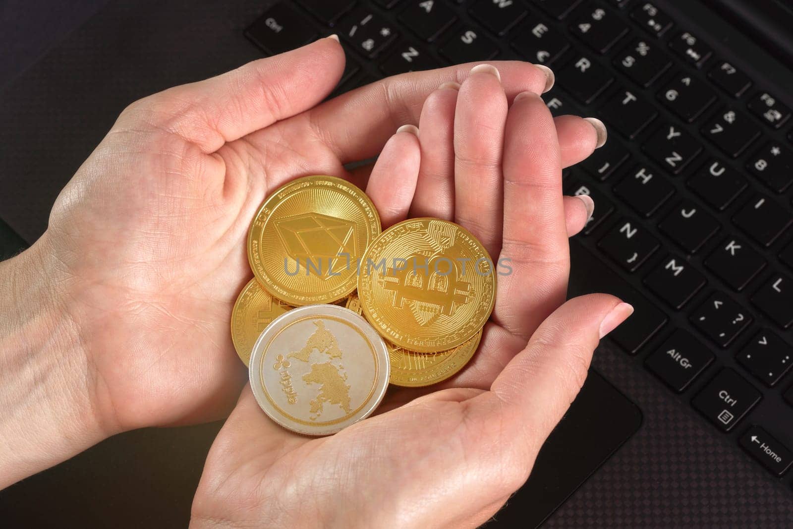 Woman hands holding golden coloured bitcoin, ripple and ethereum cryptocurrency coins over black laptop keyboard