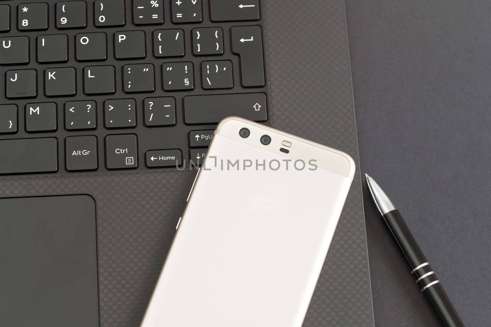 Black laptop keyboard, mobile phone and pen on gray table - view from above by Ivanko