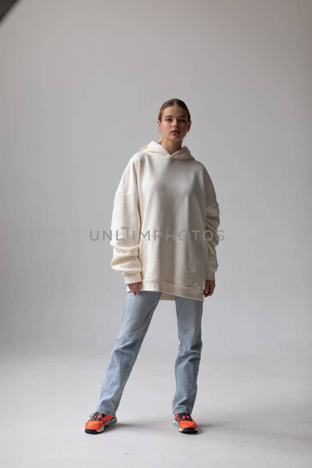 Beautiful blonde woman in a white hoodie and blue jeans posing on a white background by Freeman_Studio