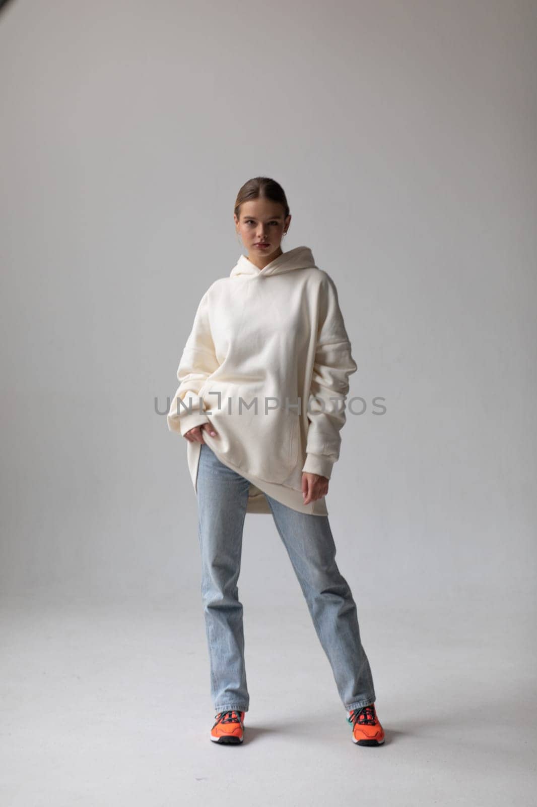 Beautiful blonde woman in a white hoodie and blue jeans posing on a white background by Freeman_Studio