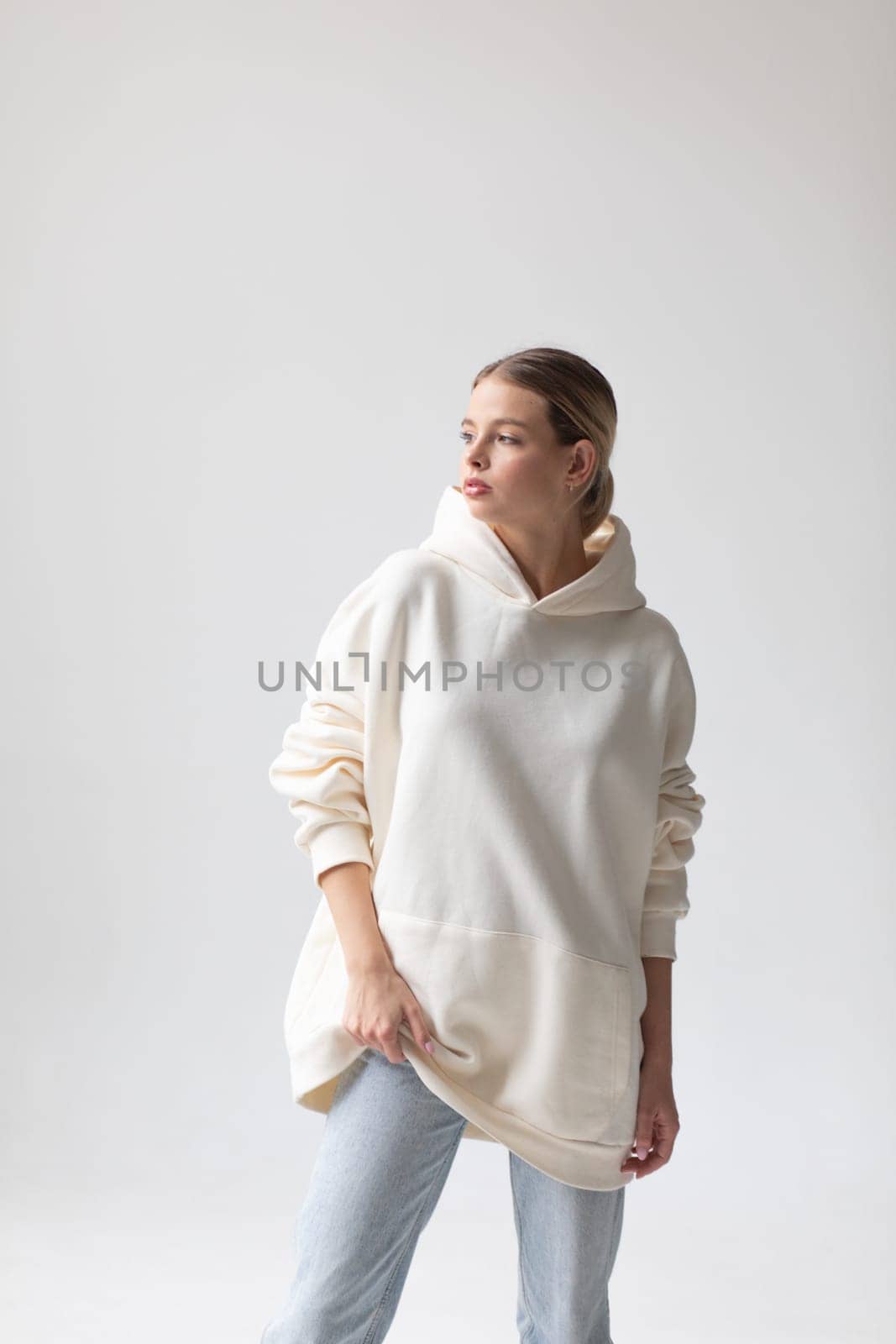 Beautiful blonde woman in a white hoodie and blue jeans posing on a white background by Freeman_Studio