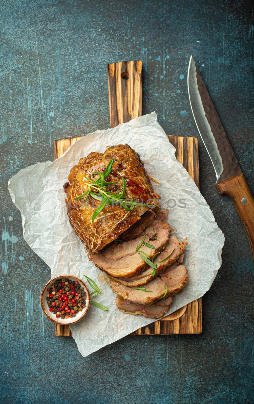 Rolled turkey roasted with spices and herbs on baking paper with knife and rustic concrete background top view. Baked cut for slices turkey fillet roll for dinner by its_al_dente