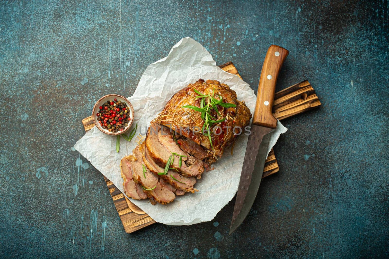 Rolled turkey roasted with spices and herbs on baking paper with knife and rustic concrete background top view. Baked cut for slices turkey fillet roll for dinner.