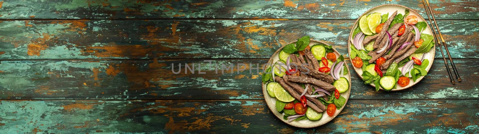 Two plates with traditional Thai beef salad with vegetables and mint top view served on rustic wooden background, healthy exotic asian meal by its_al_dente