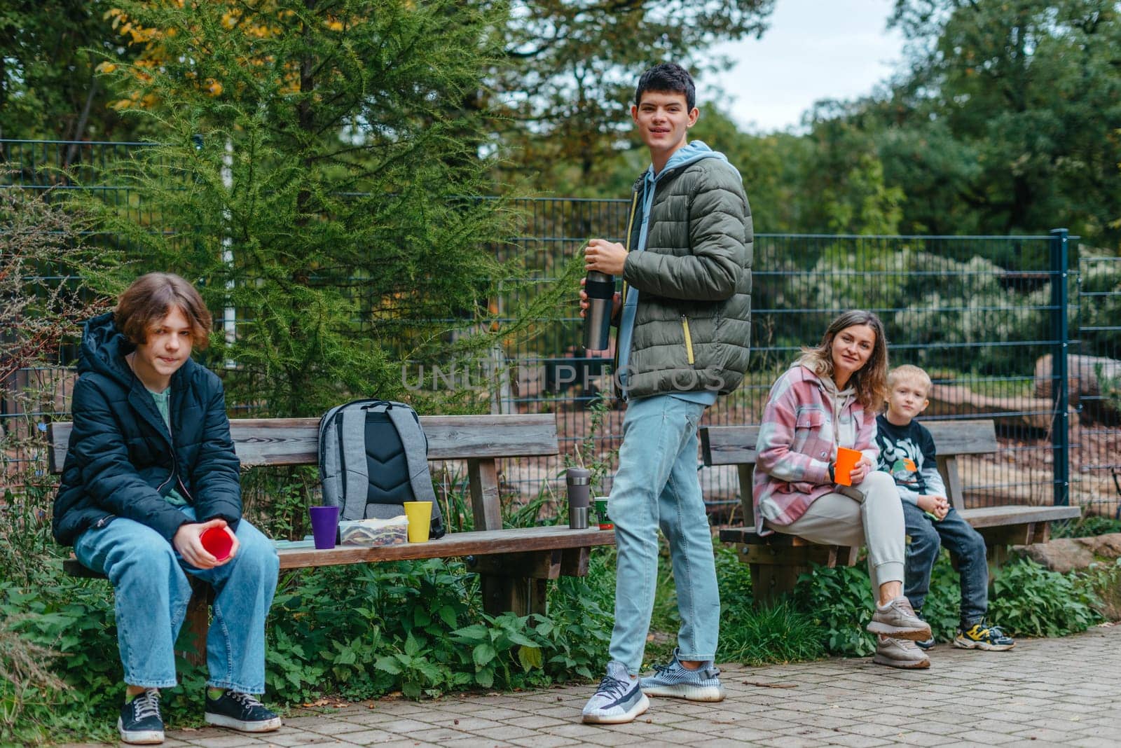 Happy Family drinking tea from a thermos in the forest. Photo of cute charming mother with childrens dressed casual outfit walking sitting bench drinking tea smiling outside city park by Andrii_Ko