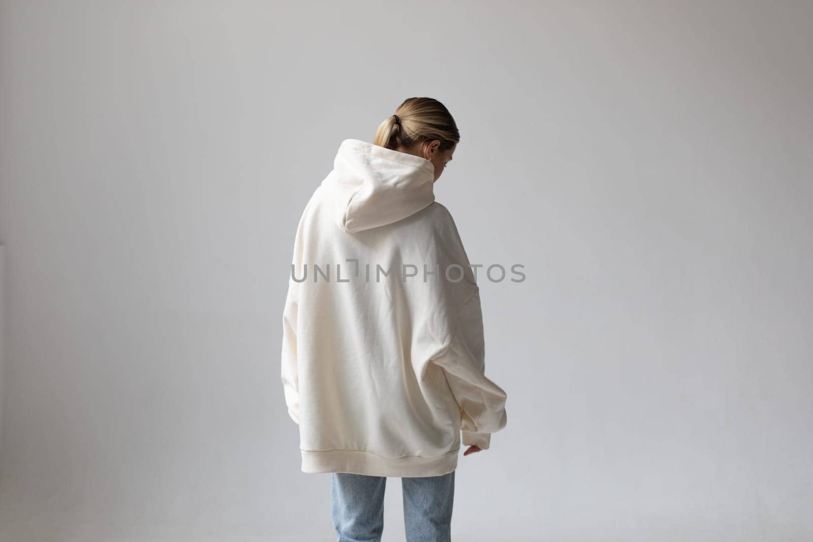 Beautiful blonde woman in a white hoodie and blue jeans posing on a white background. High quality photo