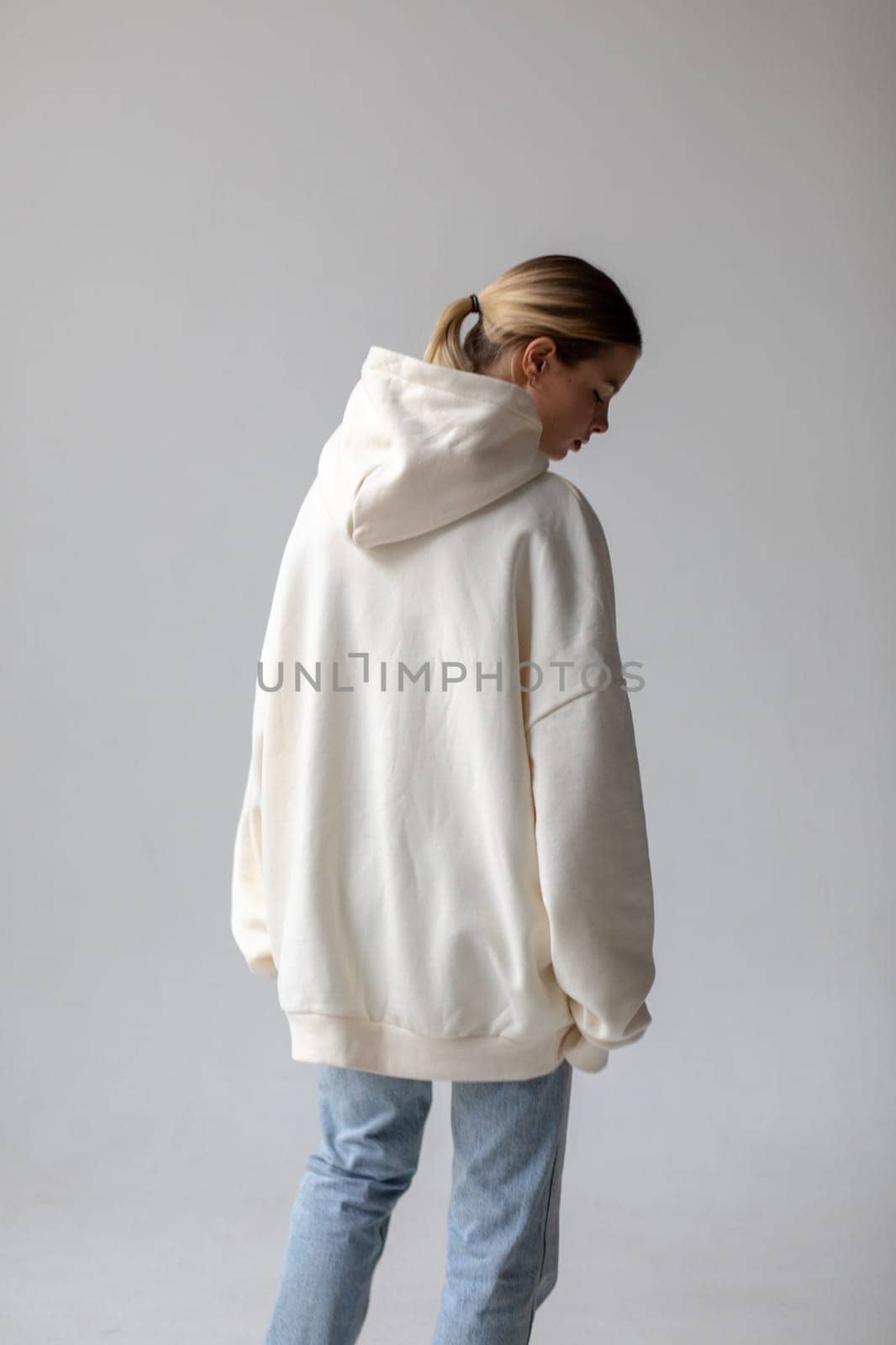 Beautiful blonde woman in a white hoodie and blue jeans posing on a white background by Freeman_Studio