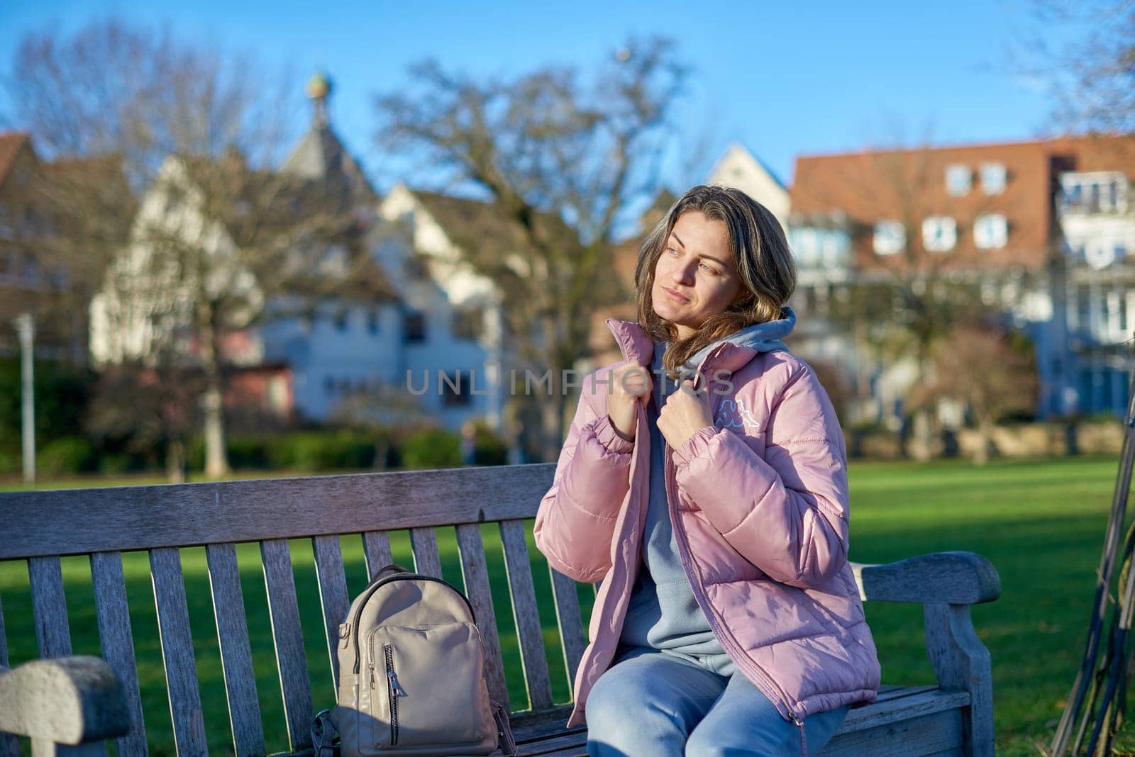 Winter Wonderland Elegance: Beautiful Girl in Pink Jacket Enjoys Festive Atmosphere in Bitigheim-Bissingen Park. Experience the magic of the holiday season as a charming girl in a pink winter jacket sits on a bench in a park against the backdrop of the historic town of Bitigheim-Bissingen, Baden-Württemberg, Germany. The scene is adorned with picturesque half-timbered houses, creating a delightful blend of winter charm and architectural beauty.