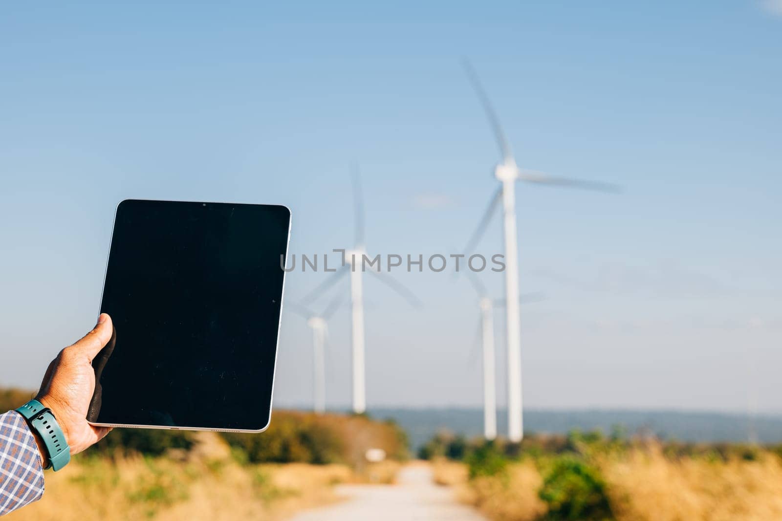 Technician tablet in hand at windmill farm. Engineer ensures clean energy. Expertise in turbine efficiency and global electricity control portrayed confidently.
