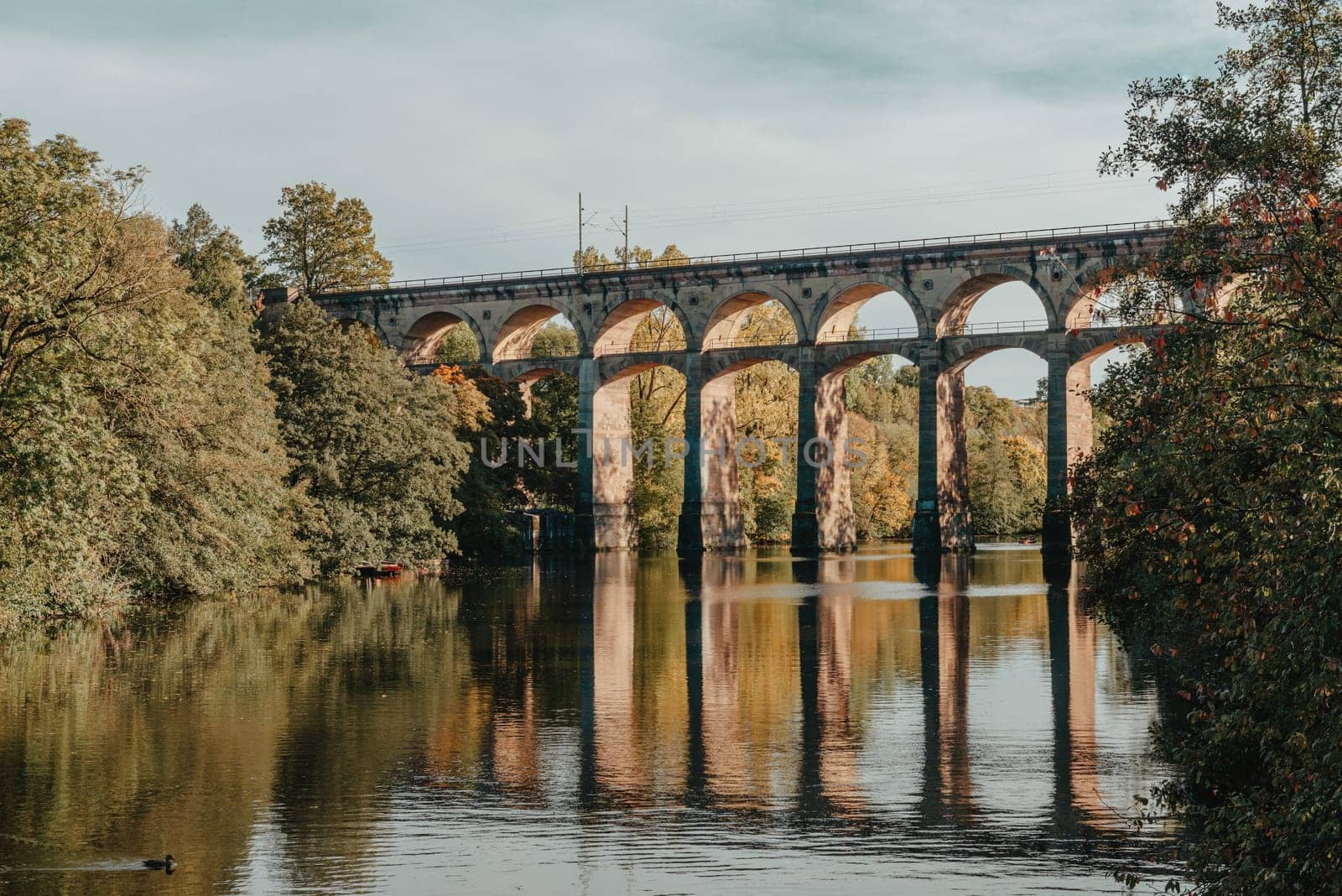 Railway Bridge with river in Bietigheim-Bissingen, Germany. Autumn. Railway viaduct over the Enz River, built in 1853 by Karl von Etzel on a sunny summer day. Bietigheim-Bissingen, Germany. Old viaduct in Bietigheim reflected in the river. Baden-Wurttemberg, Germany. Train passing a train bridge on a cloudy day in Germany by Andrii_Ko