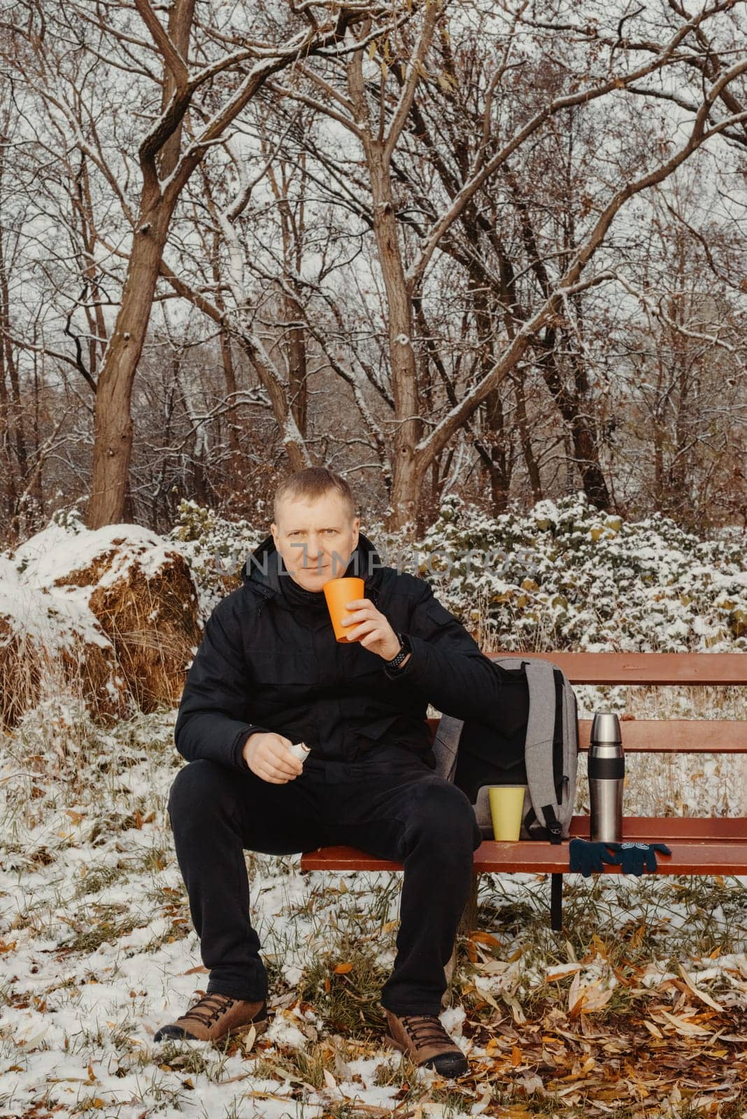 Winter Serenity: 40-Year-Old Man Enjoying Tea on Snow-Covered Bench in Rural Park. Immerse yourself in the tranquil beauty of winter as a 40-year-old man finds solace on a snowy bench in a rural park. by Andrii_Ko