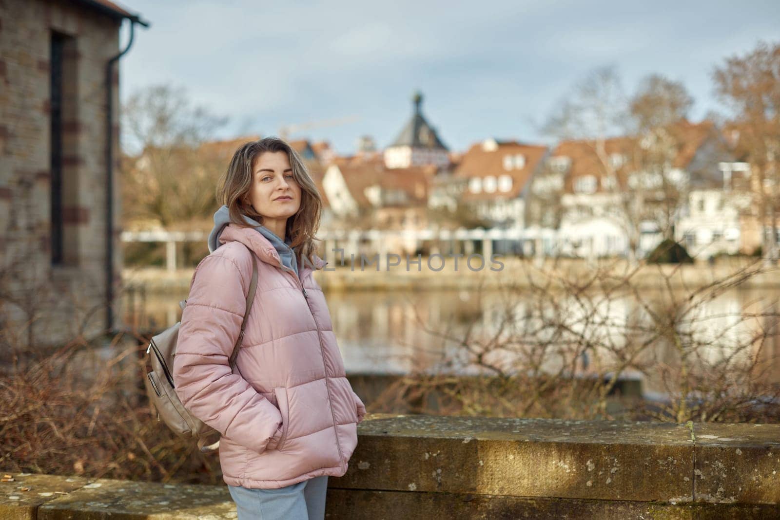 Young beautiful pretty tourist girl in warm hat and coat with backpack walking at cold autumn in Europe city enjoying her travel in Bietigheim-Bissingen, Deutschland. Outdoor portrait of young tourist woman enjoying sightseeing by Andrii_Ko