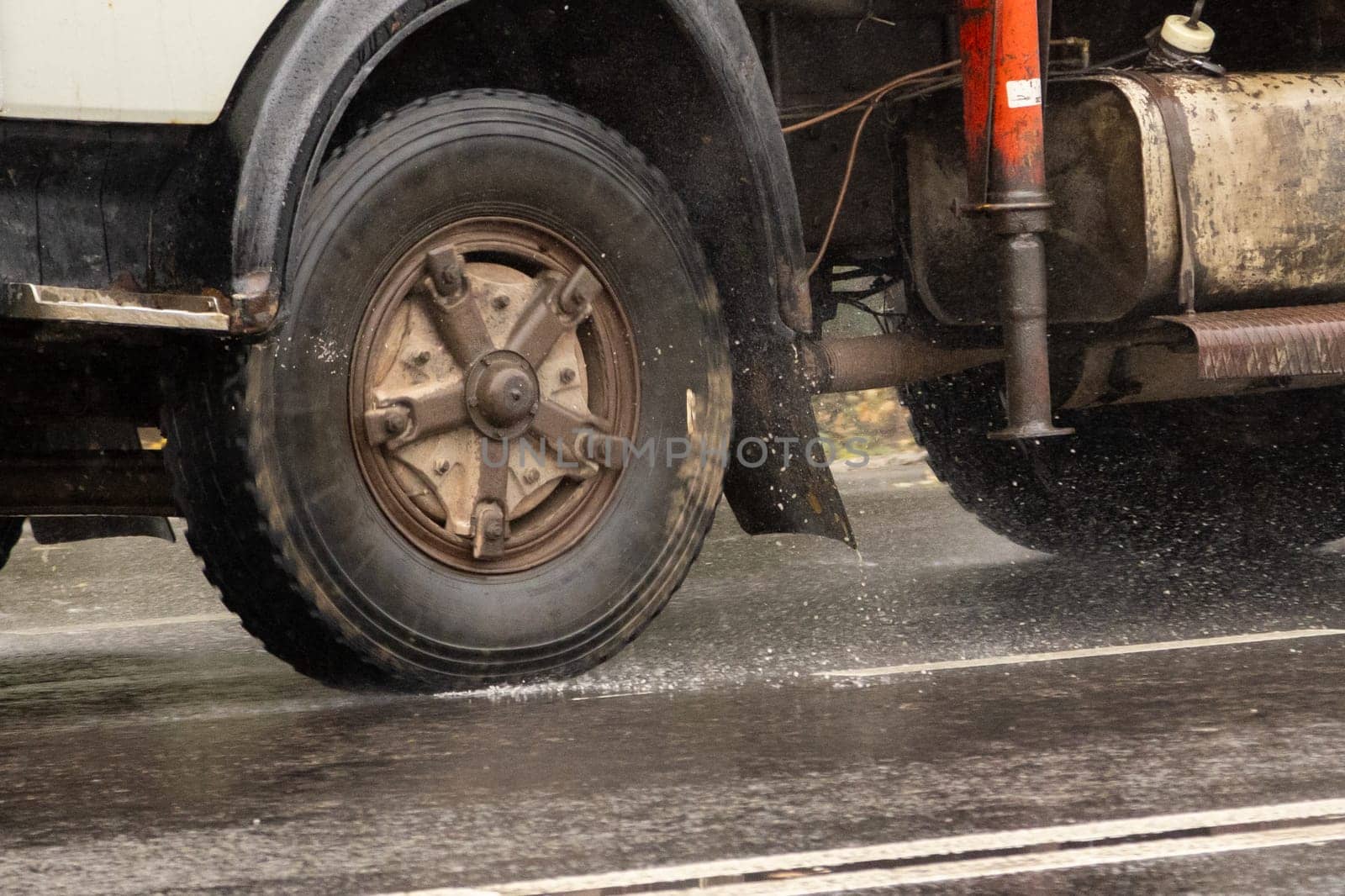 Close up of truck tire rolling on wet asphalt road, with some splashes at rainy day.