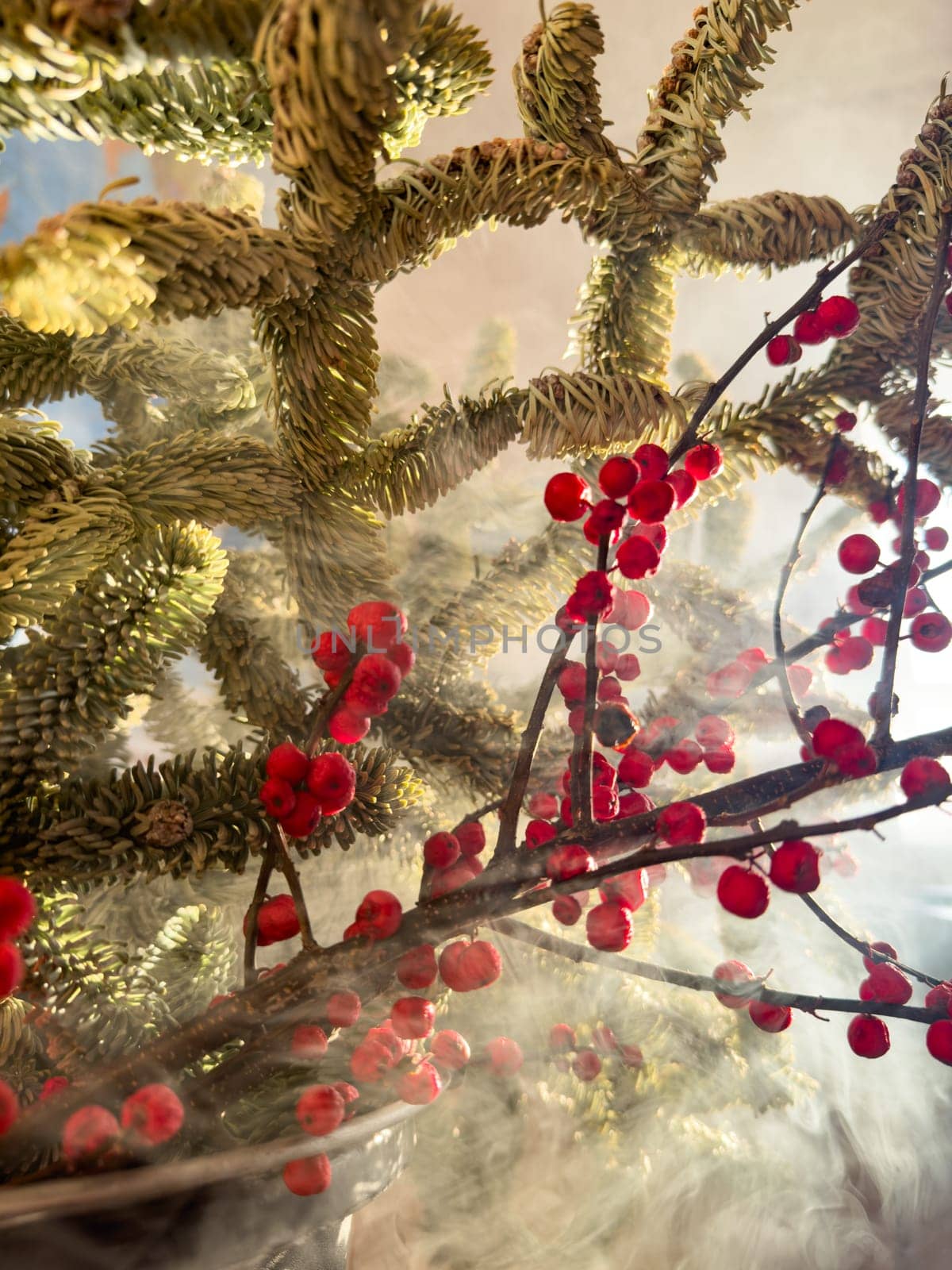 a bouquet of branches with red berries and fir branches in smoke in sunny weather, the rays of the sun through the branches. High quality photo