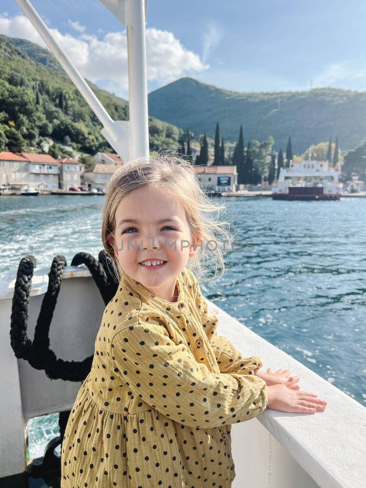 Little girl stands leaning on the side of a boat floating on the sea towards a mountainous shore. High quality photo