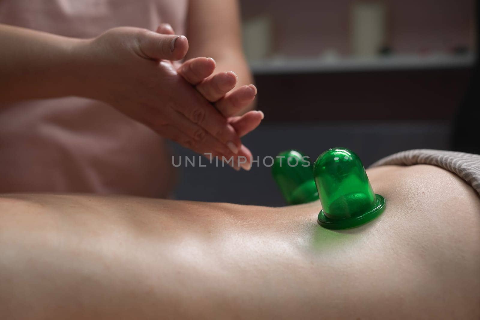 A woman undergoes an anti-cellulite massage procedure using a vacuum jar. Close-up of the lower back. by mrwed54