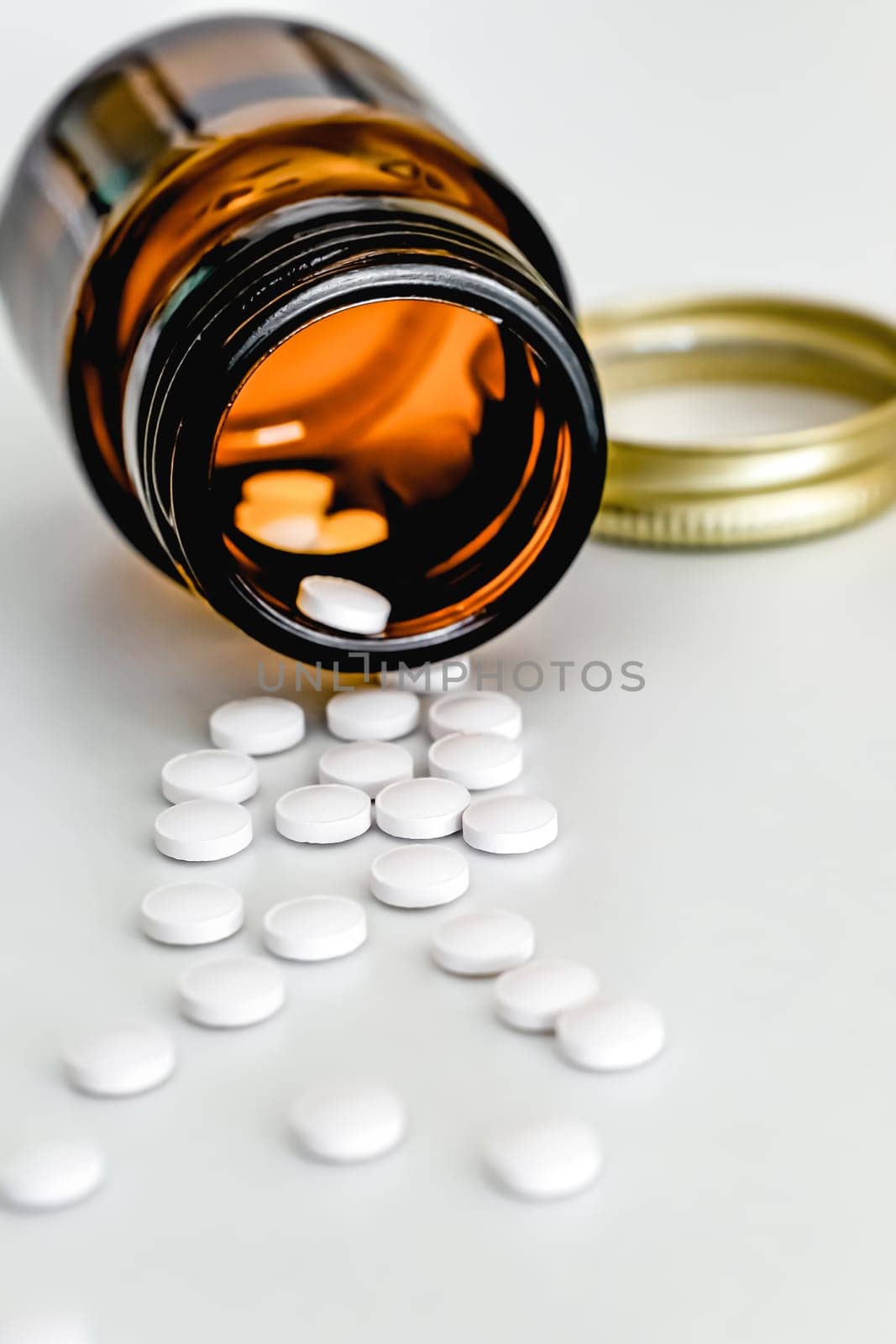 White Tablets Scattered on Table Next to Brown Glass Vial, on White Background, Close-up, Vertical Frame