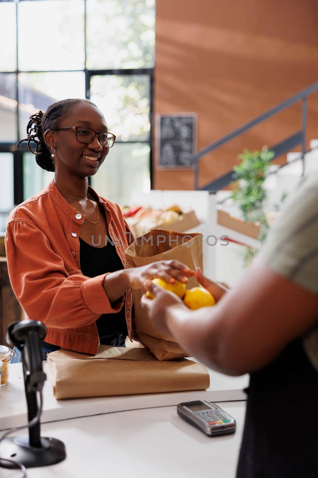 African American women presenting recently picked lemons at the cashier desk. Image showcasing a female customer offering fruits to a black vendor to weigh.