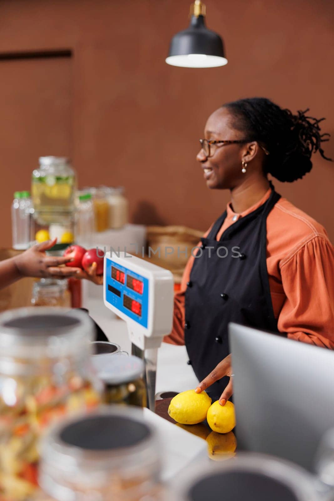 Black woman assists a customer in a grocery store, promoting locally grown and organic products. They communicate and use technology for an efficient checkout process in the eco-friendly market.