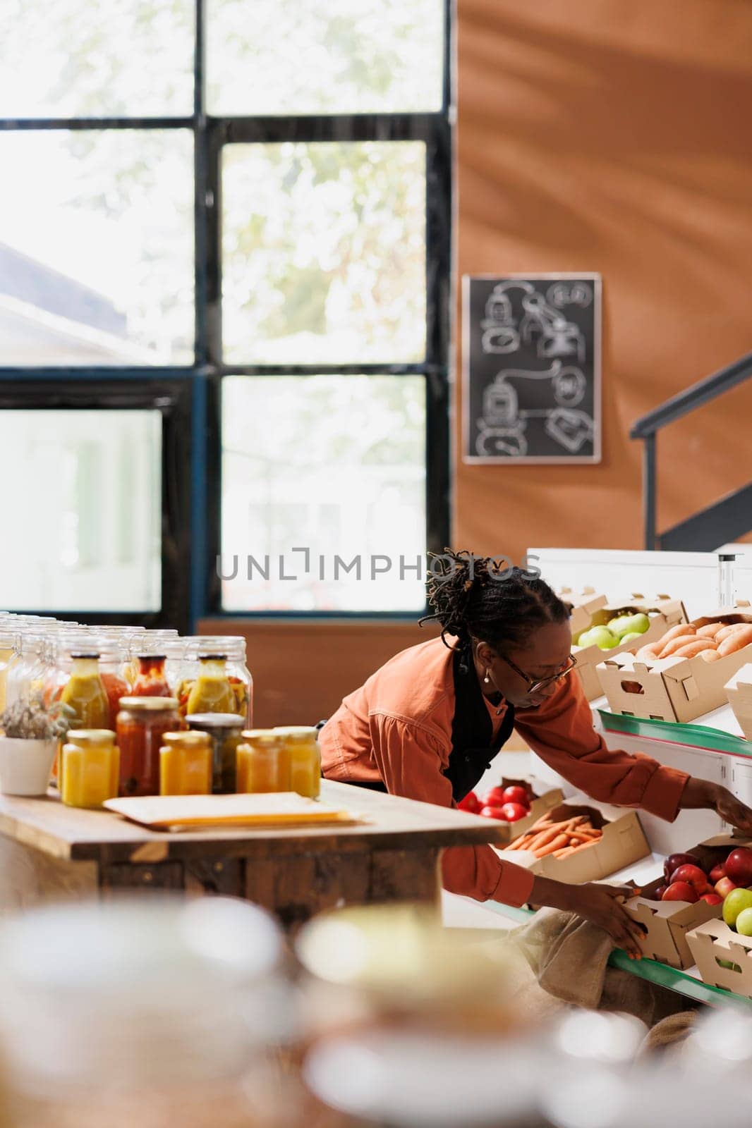 Vendor setting up an environmentally friendly business that sells bulk goods, plastic free packaging, and fresh produce. Black woman stocking shelves with boxes of produce and fruits from farms.