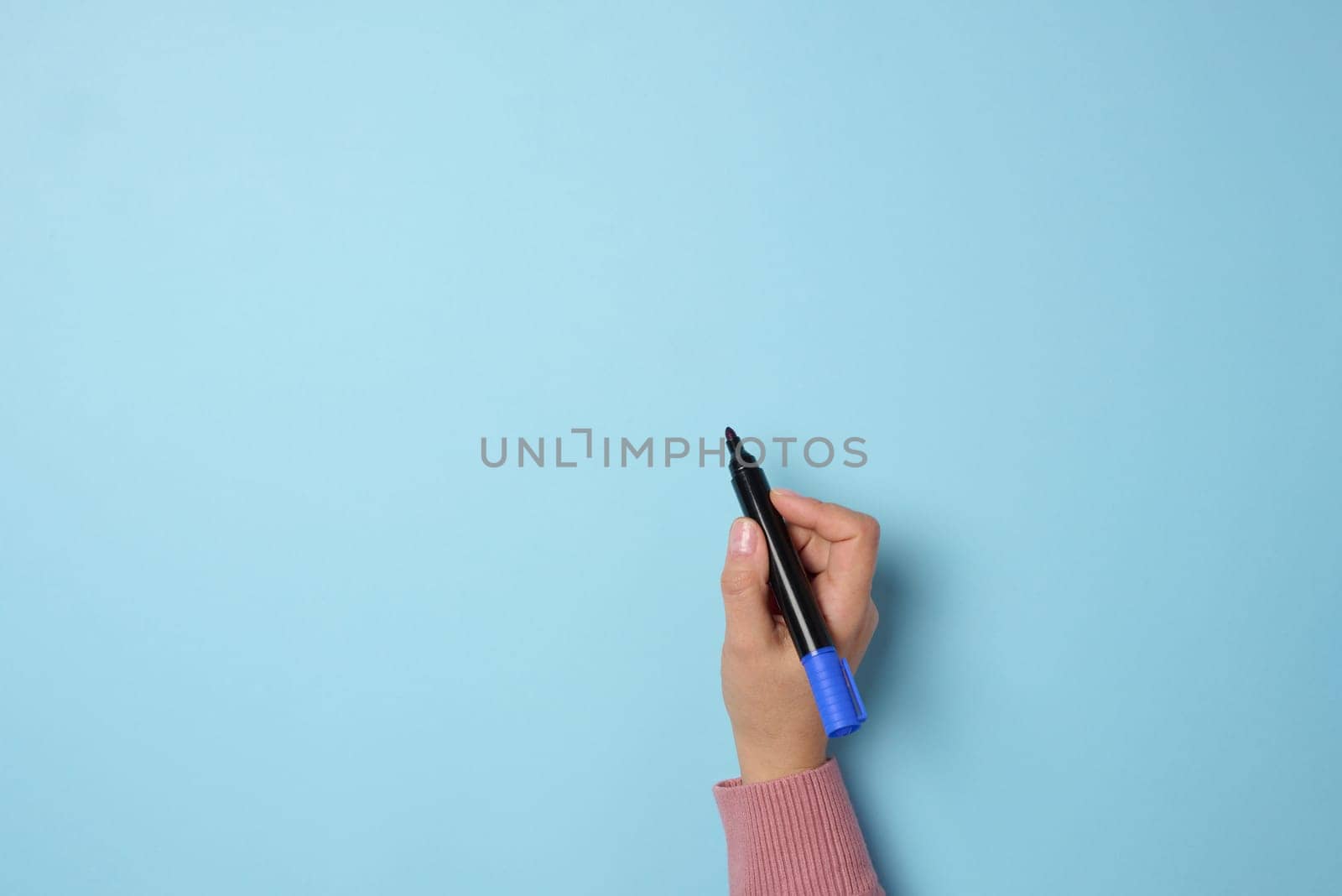 A woman's hand holds a blue felt-tip pen on a blue background, space for an inscription by ndanko