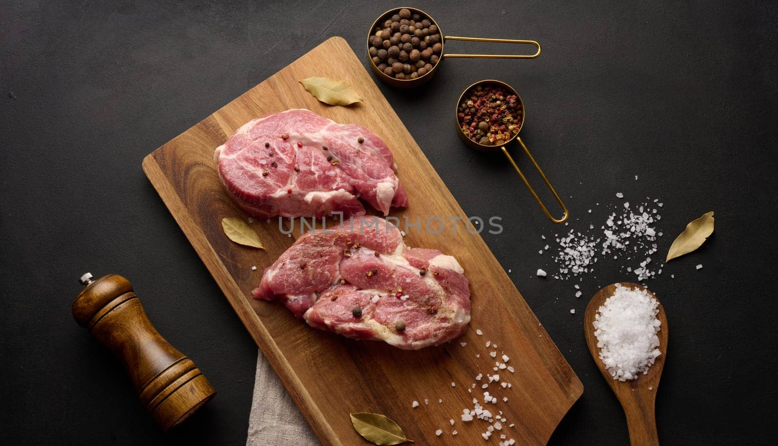 Two raw pork neck steaks on a board and spices for cooking. Top view by ndanko