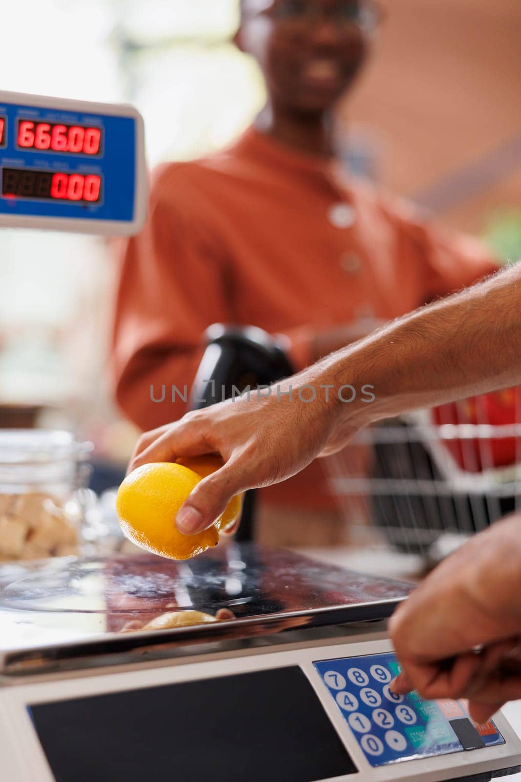 Close-up of vendor placing lemons on scale to confirm price for african american female customer. Male shopkeeper weighing freshly harvested fruits and vegetables for the client.