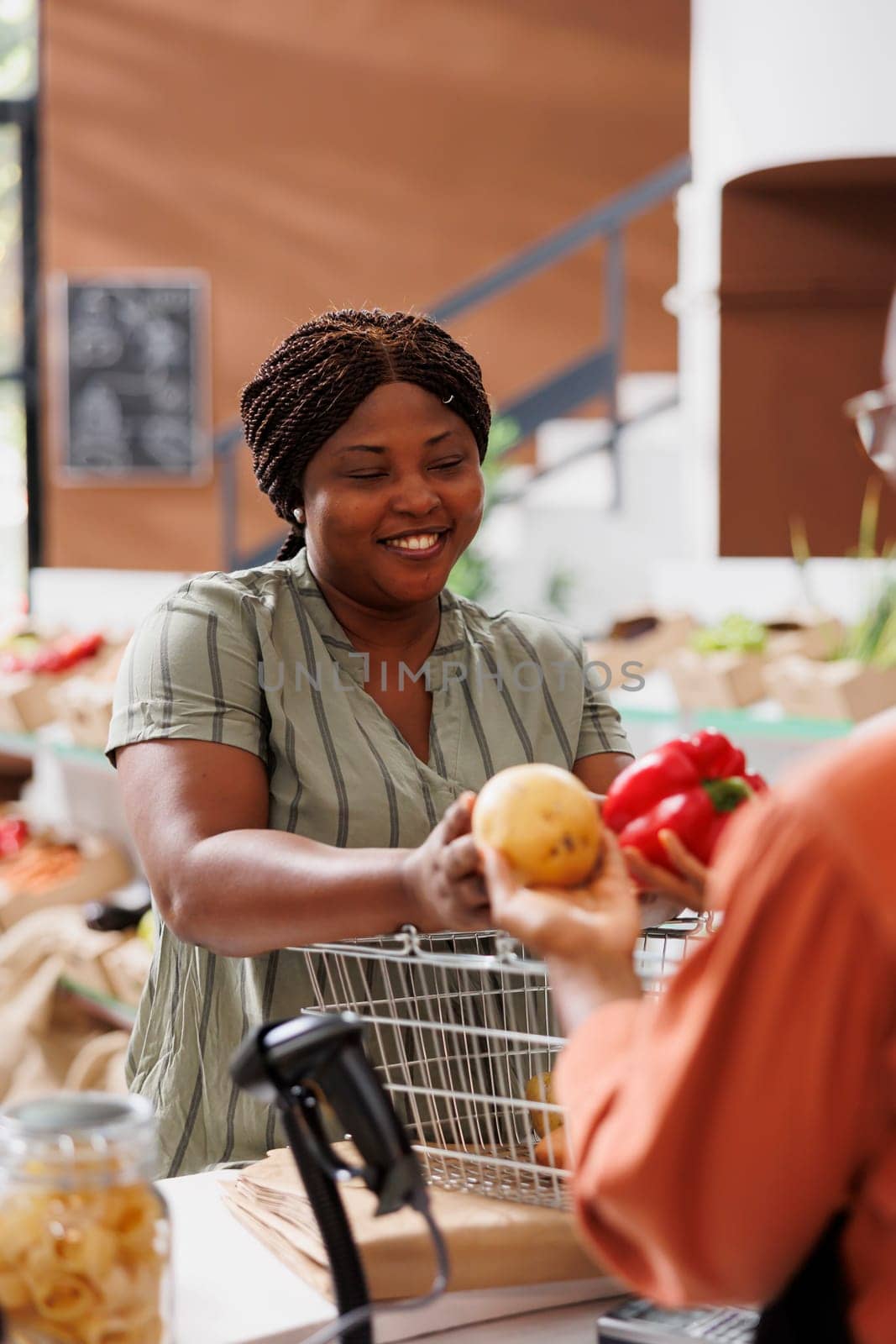 Happy african american female individual shopping for locally grown organic vegetables for healthy recipes. Young consumer giving local vendor the fresh produce for weighing and packaging.