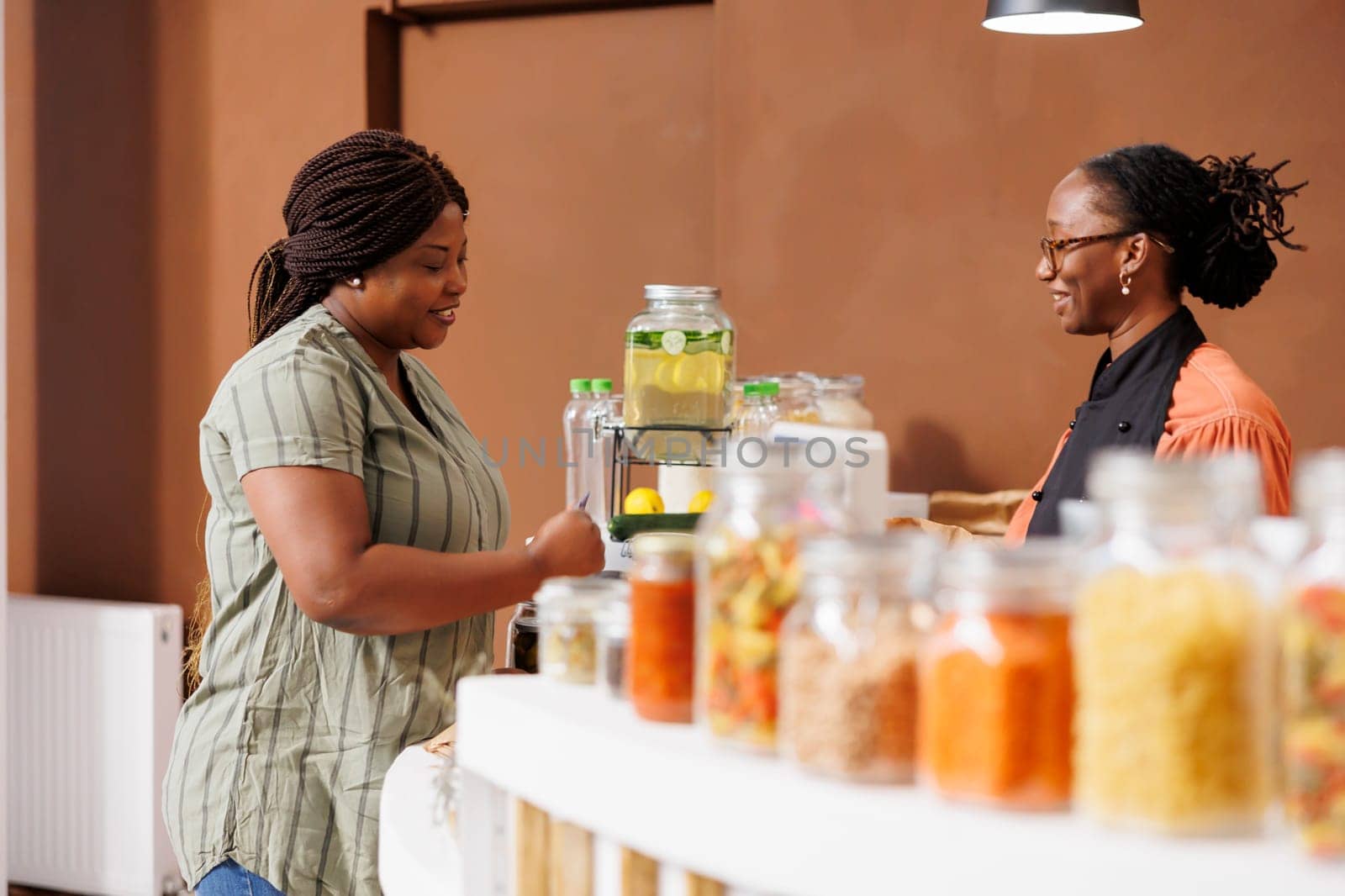 Smiling black woman shops at bio food market, buying fresh organic produce and supporting sustainable practices and zero waste. Female customer preparing to pay for her sustainable products.