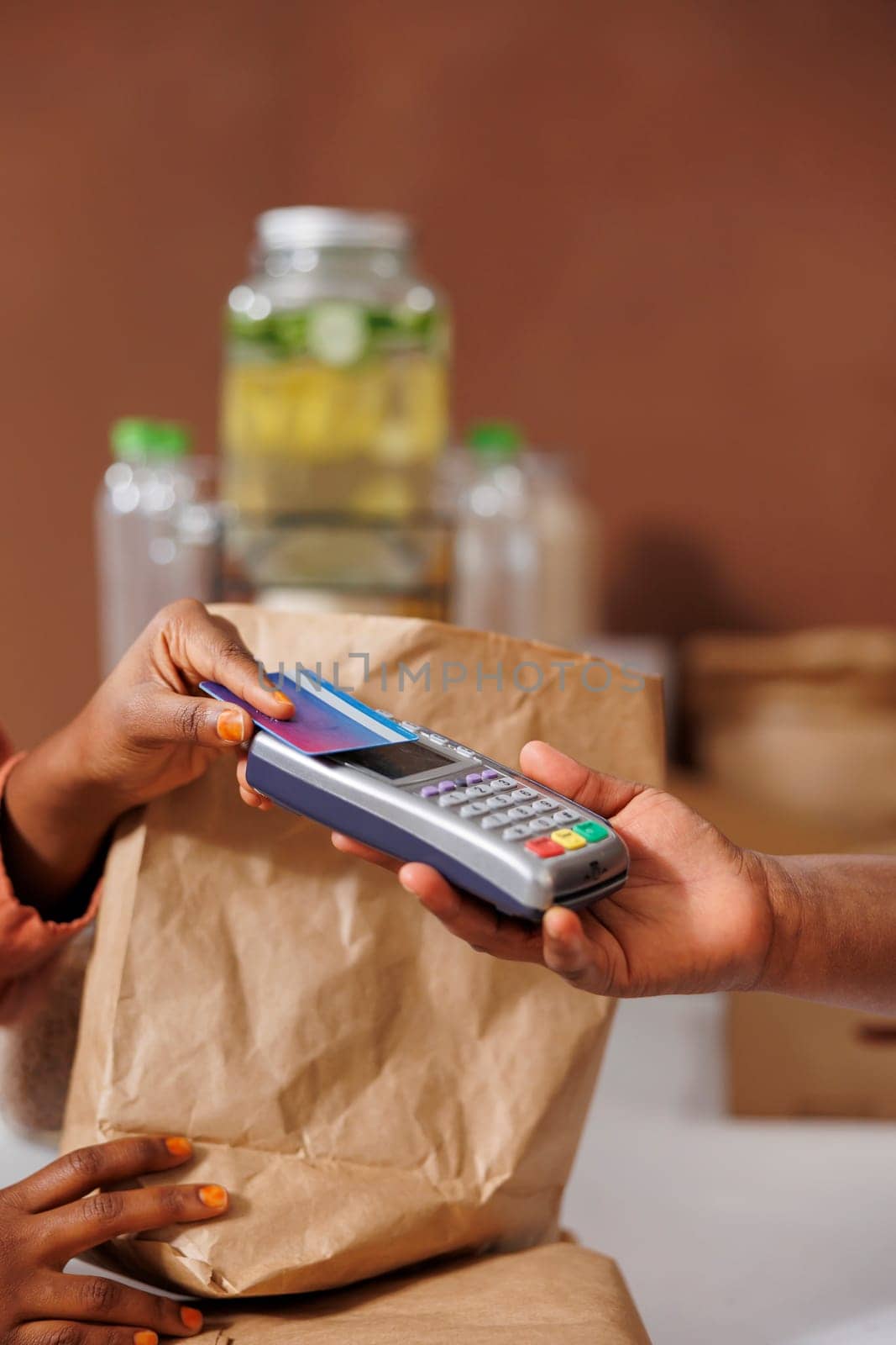 Detailed image of african american female customer paying with a credit card at the checkout counter. Closeup shot of black vendor holding the pos machine for the client to make cashless payment.