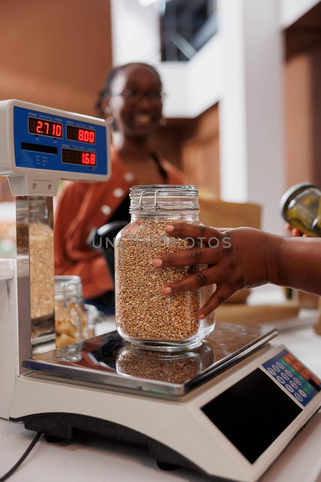 Closeup of black person assists customer with weighing fresh produce on digital scale at eco friendly store, promoting healthy, locally grown items. Seller measures sustainable additives free product.