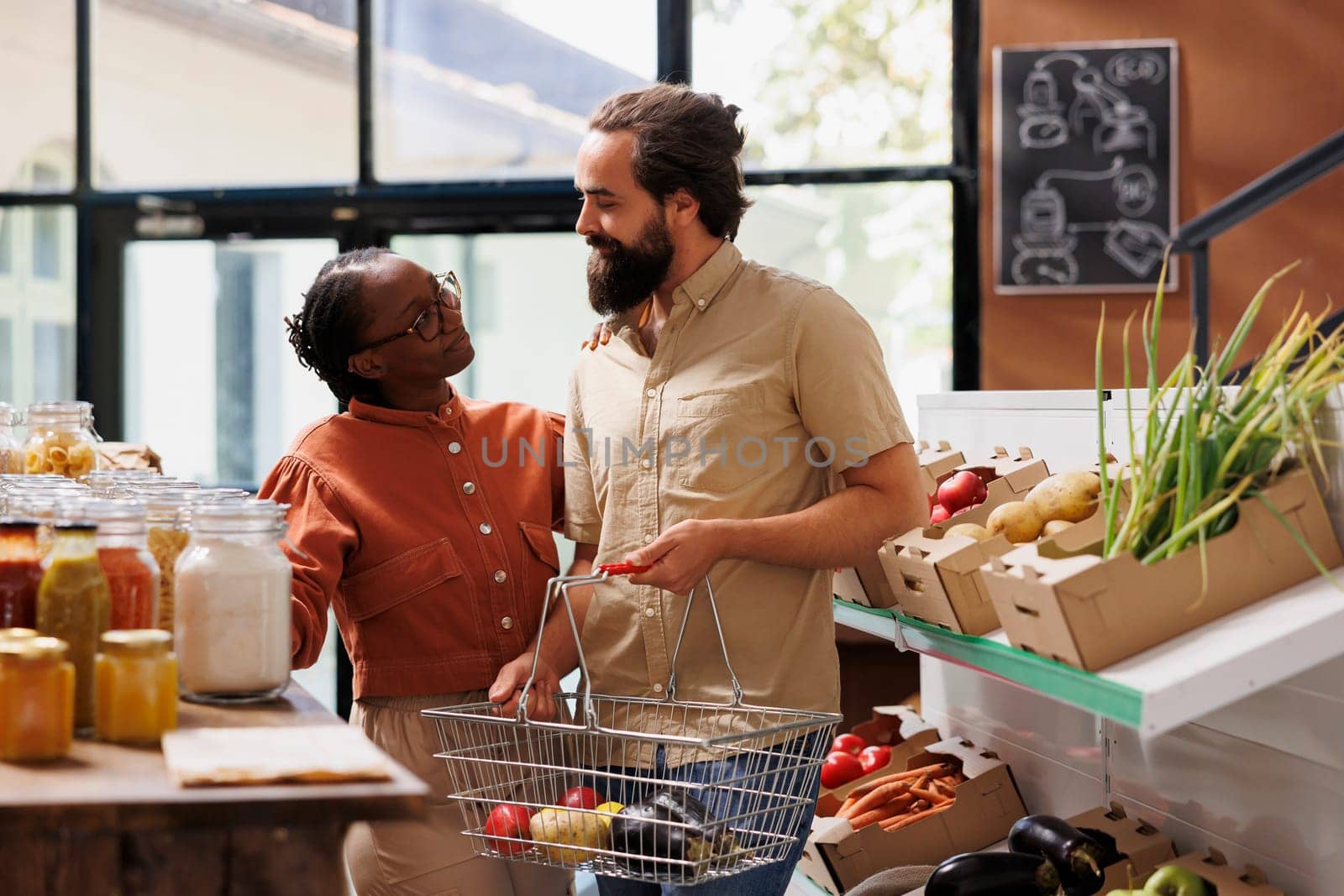 Happy multicultural couple browsing in sustainable eco friendly store. African american woman and caucasian man with a basket searching bio food products for a healthy lifestyle.