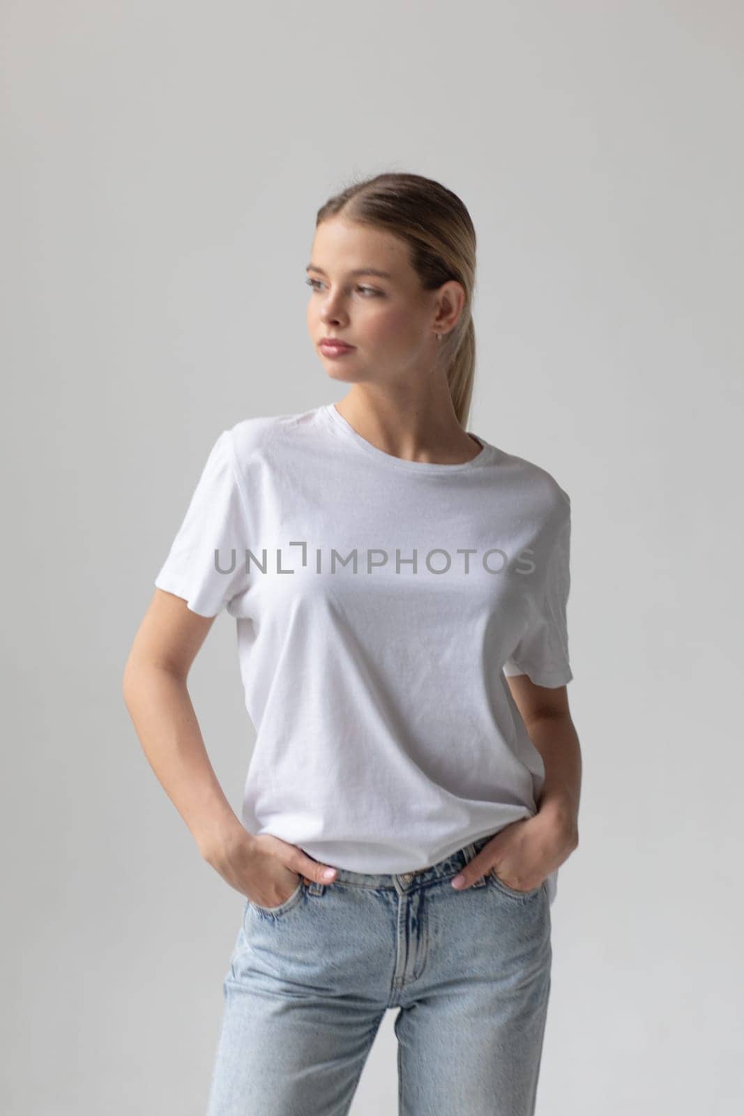 Beautiful blonde woman in a white T-shirt and blue jeans posing on a white background by Freeman_Studio