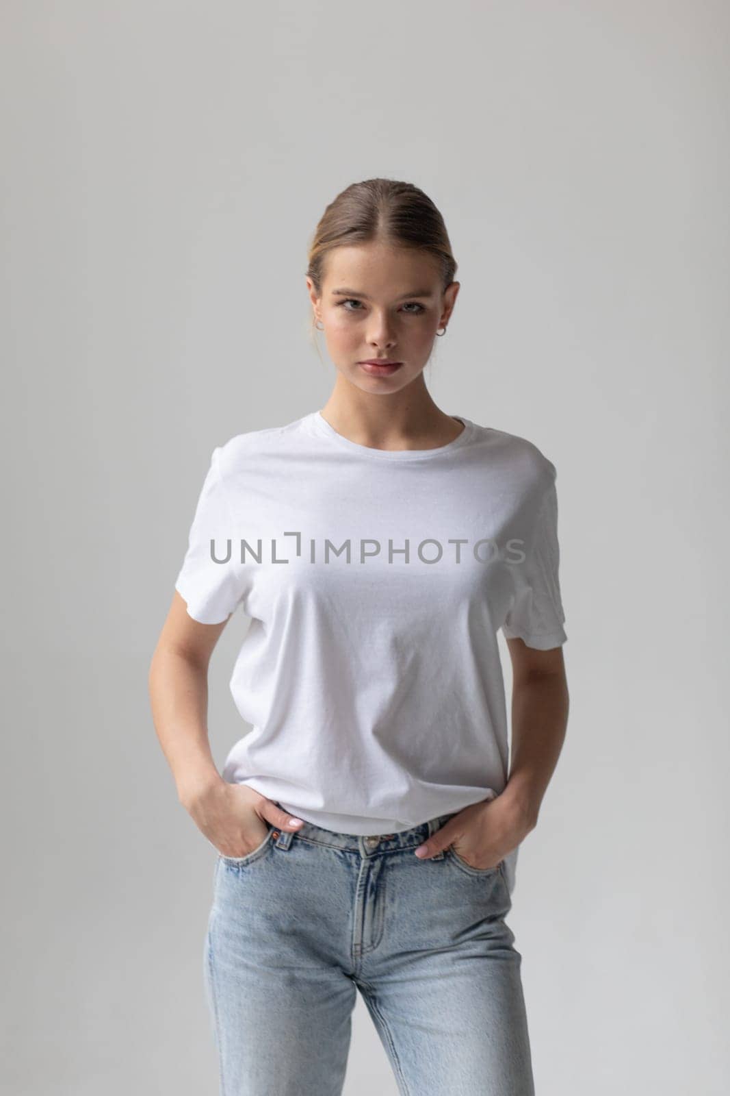 Beautiful blonde woman in a white T-shirt and blue jeans posing on a white background by Freeman_Studio