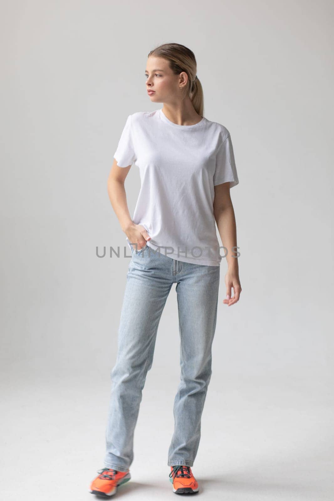 Beautiful blonde woman in a white T-shirt and blue jeans posing on a white background by Freeman_Studio