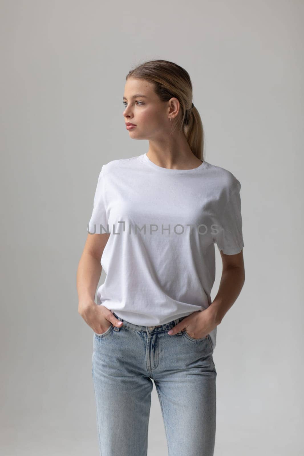 Beautiful blonde woman in a white T-shirt and blue jeans posing on a white background by Freeman_Studio