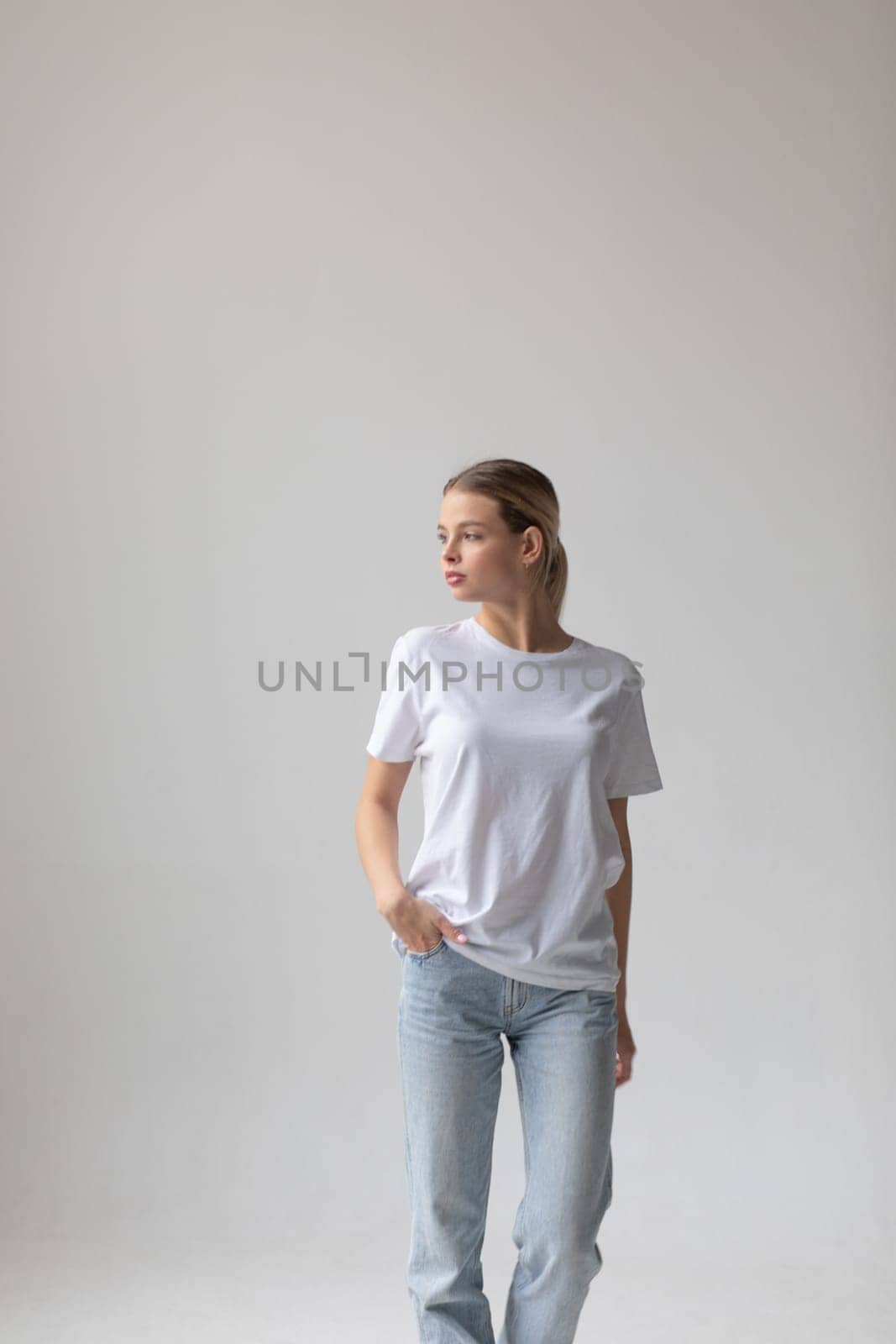 Beautiful blonde woman in a white T-shirt and blue jeans posing on a white background by Freeman_Studio