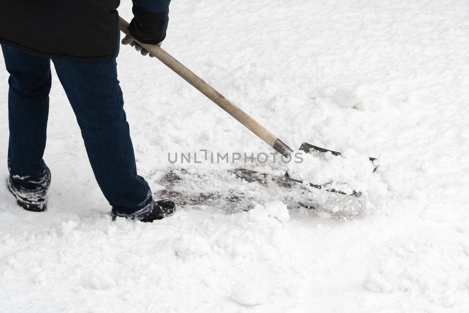 A hardworking man clearing away the freshly fallen snow with his trusty iron shovel, complete with a sturdy wooden handle. A close-up view of the snow removal process