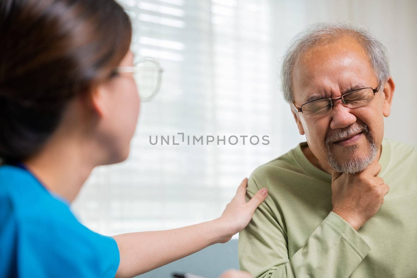 Asian young nurse checking senior man neck pain in clinic at retirement home by Sorapop