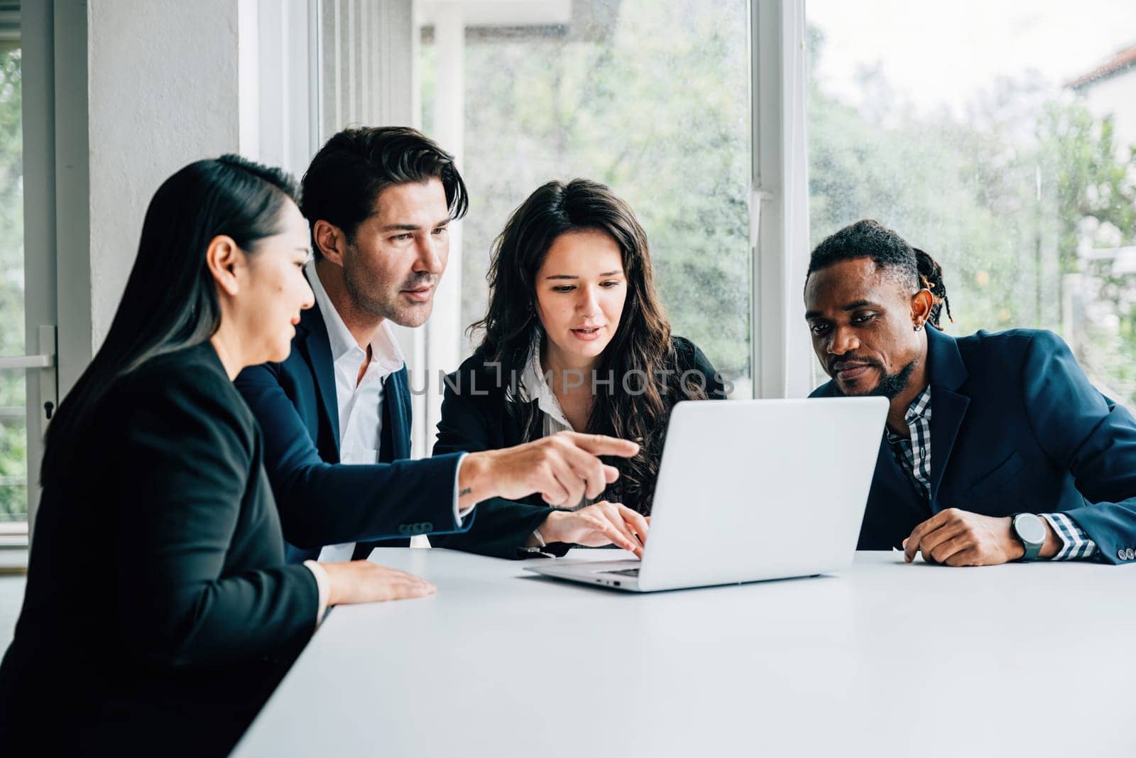 Diverse business professionals, both men and women, work together in meeting room using laptop. Their teamwork, collaboration, diversity are apparent they discuss, plan, and strategize for success.