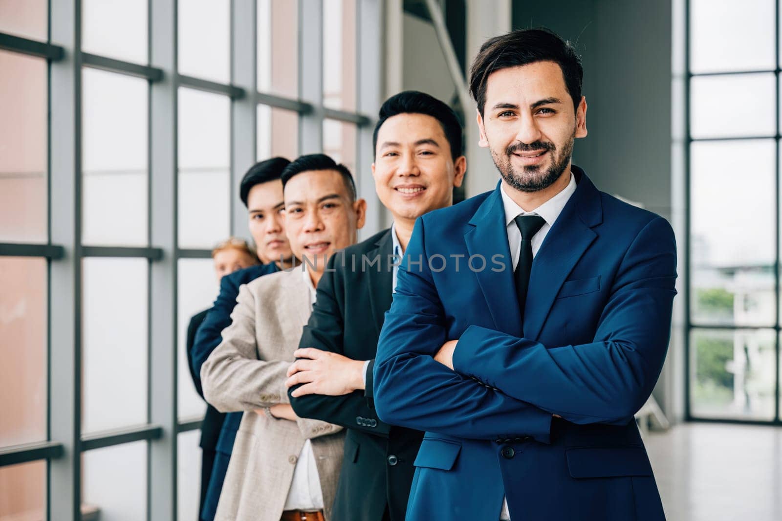 Young businesspeople and a businessman gather indoors, standing with crossed arms in the office. Their unity, success, and teamwork shine in this dynamic group portrait. by Sorapop