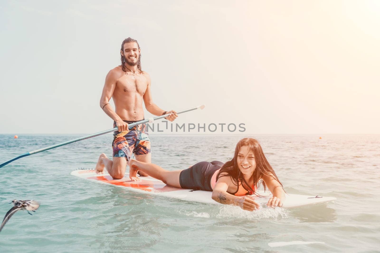 Silhouette of woman standing, surfing on SUP board, confident paddling through water surface. Idyllic sunset or sunrise. Sports active lifestyle at sea or river.