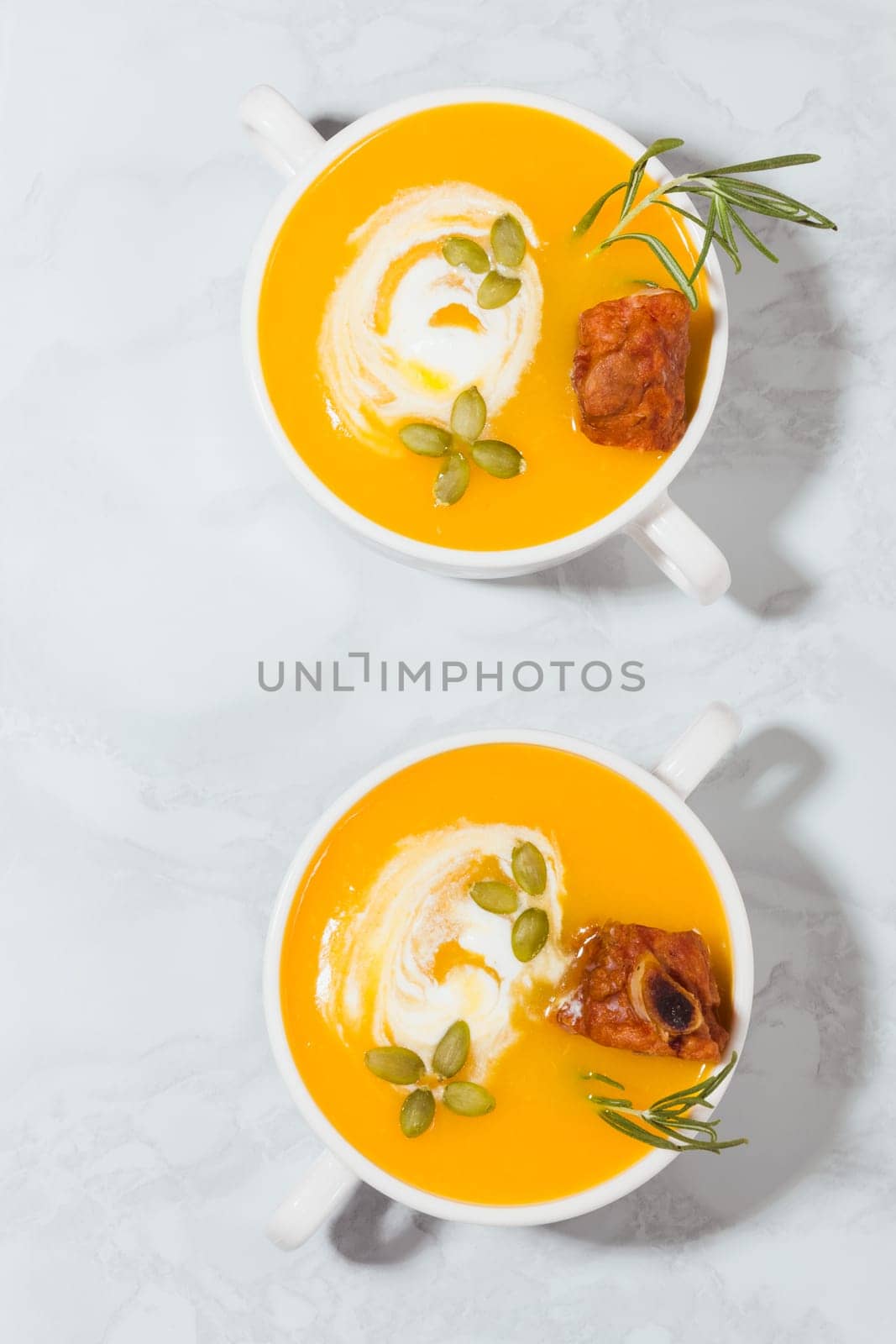 Pumpkin cream soup with smoked pork ribs and cream in two plates close-up, top view
