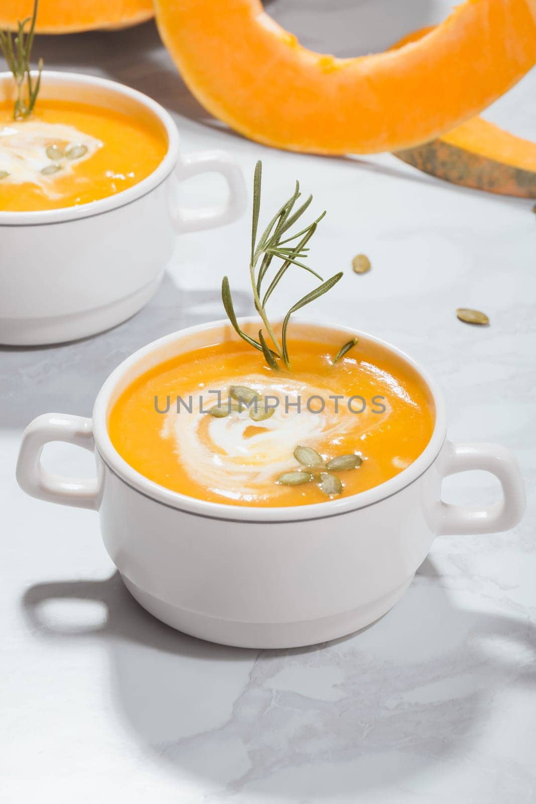 Pumpkin cream soup with sour cream, seeds and rosemary in a plate on a pumpkin background