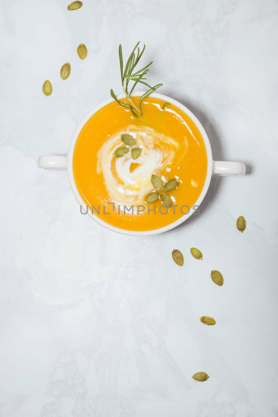 Pumpkin cream soup with sour cream, seeds and rosemary in a plate with copy space, top view by ElenaNEL