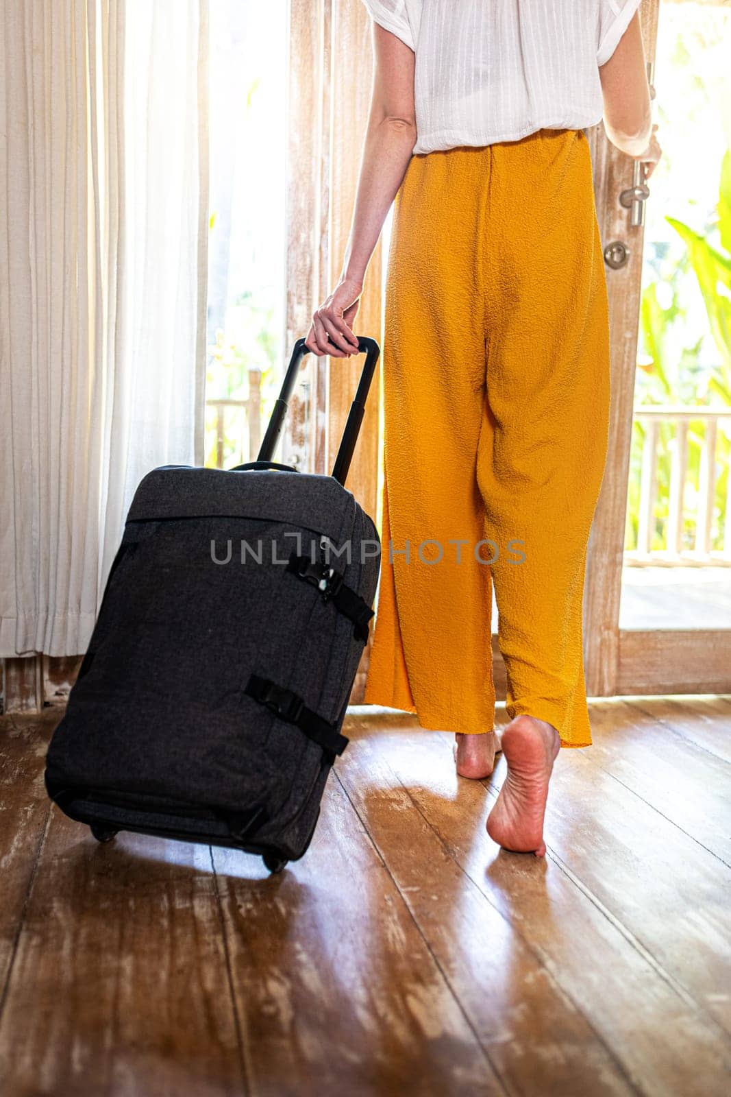 Unrecognizable woman walking out of hotel bedroom with suitcase. Vertical image. by Hoverstock