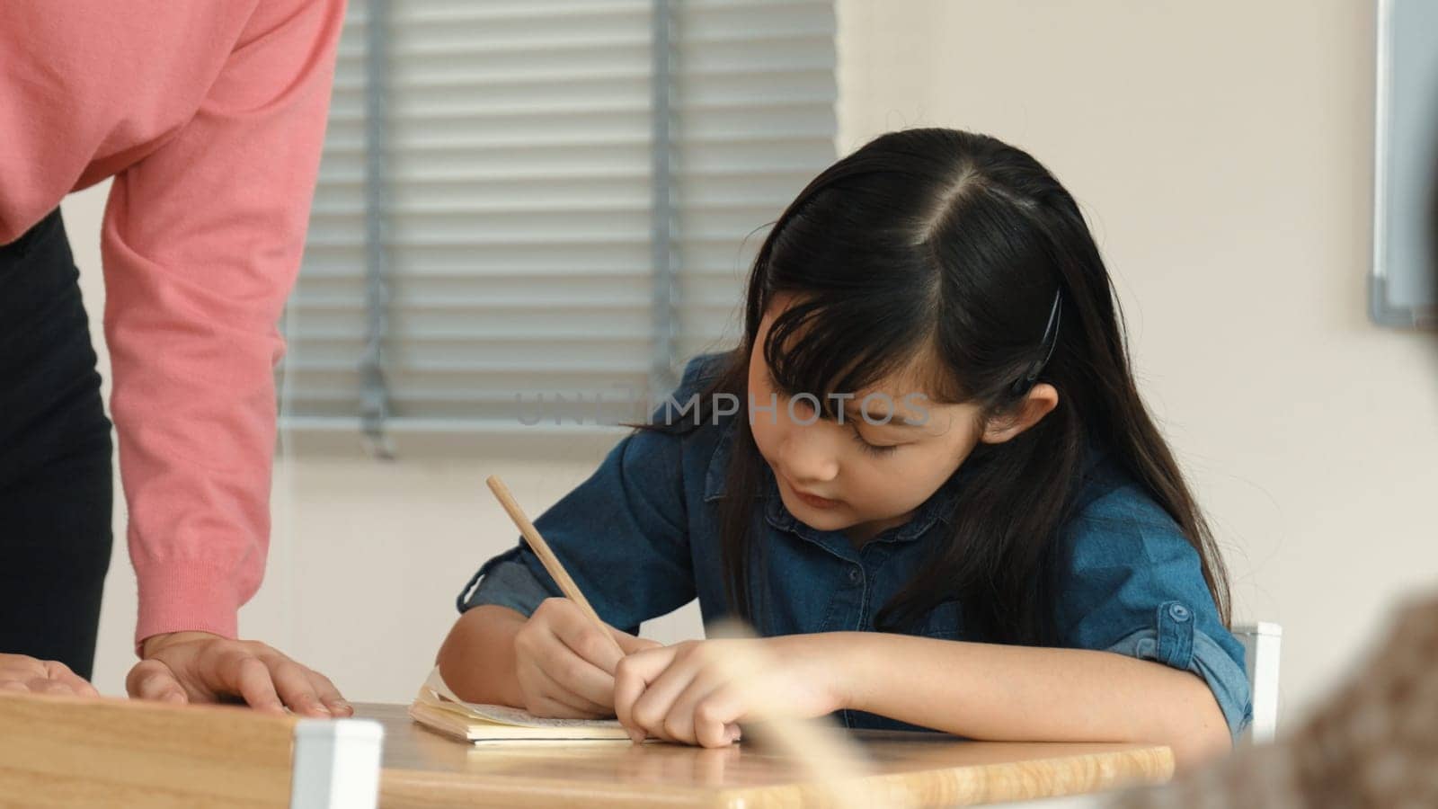 Asian girl writing or taking a note while teacher checking classwork. Pedagogy. by biancoblue