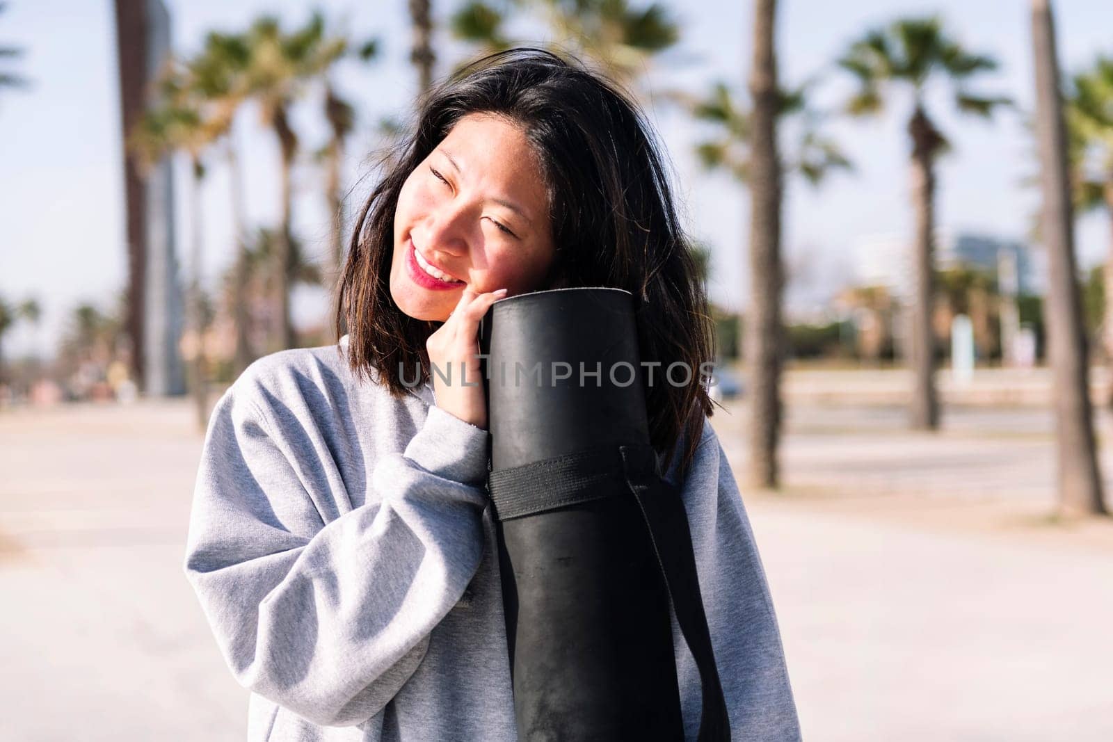 portrait of a young asian woman dressed in casual clothes smiling while holding her yoga mat, healthy and active lifestyle concept, copy space for text